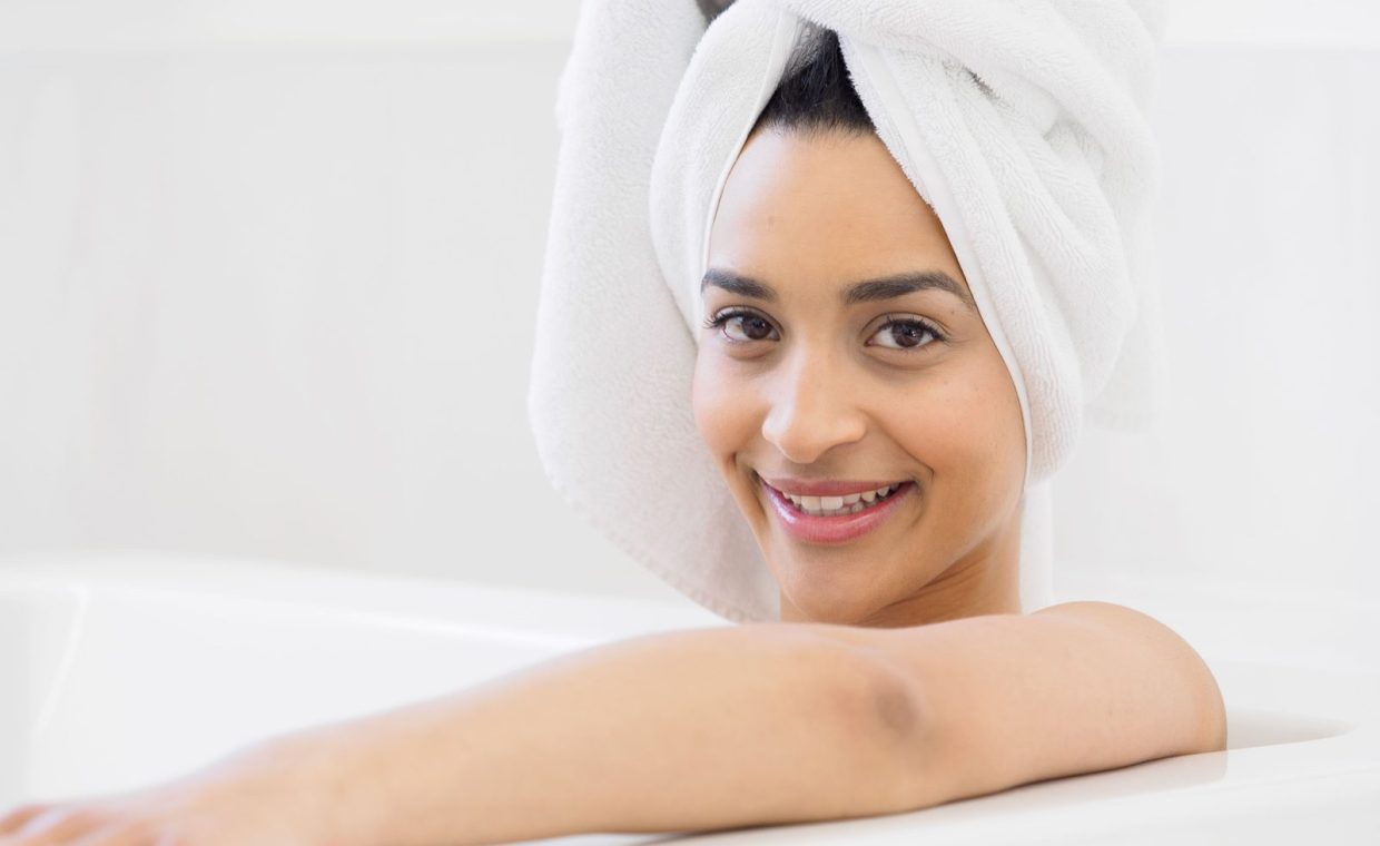 Smiling woman enjoying a relaxing bath with a towel wrapped on her head, indoors.