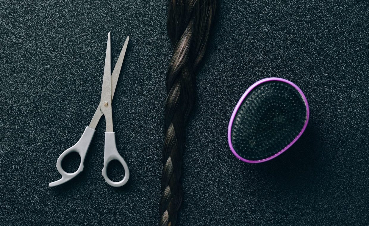 Close-up of hairdressing scissors, braided hair, and brush on black background.